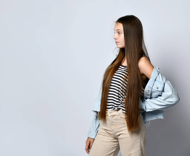 Teenage girl in striped t-shirt, denim jacket and pants. She looking at you, posing isolated on white studio background. Close up - Foto, afbeelding