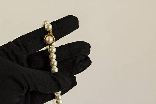 close-up shot of hand in black glove holding pearl necklace on white background - Foto, Bild