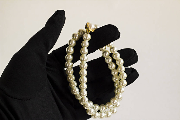 close-up shot of hand in black glove holding pearl necklace on white background - Valokuva, kuva