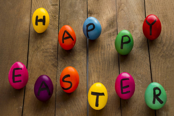 close-up shot of delicious colorful eggs with happy easter lettering on wooden tabletop - Foto, Bild