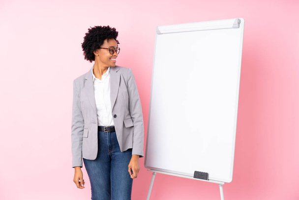 Mujer de negocios afroamericana dando una presentación en pizarra blanca sobre fondo rosa aislado mirando lado
 - Foto, imagen