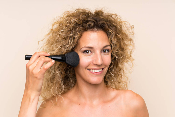 Mulher loira jovem com cabelo encaracolado com escova de maquiagem
 - Foto, Imagem