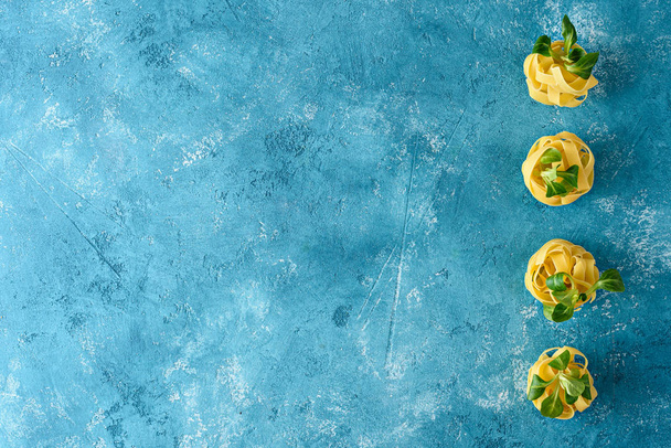 top view fresh Italian pasta, fettuccine with greens on blue background - 写真・画像
