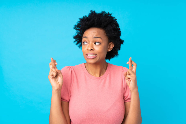 African american woman over isolated blue background with fingers crossing - Photo, Image