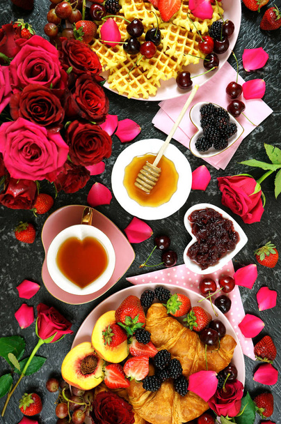 romantisches Frühstück mit Croissants, Pfannkuchen, Waffeln, Obst und Rosen. - Foto, Bild