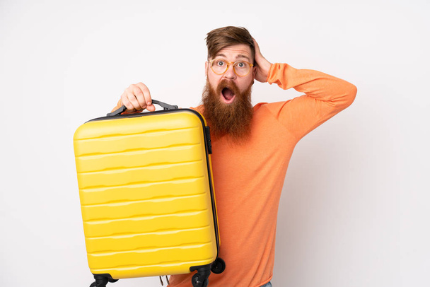 Vörös hajú férfi hosszú szakáll felett elszigetelt fehér háttér nyaralás utazási bőrönd és meglepett - Fotó, kép