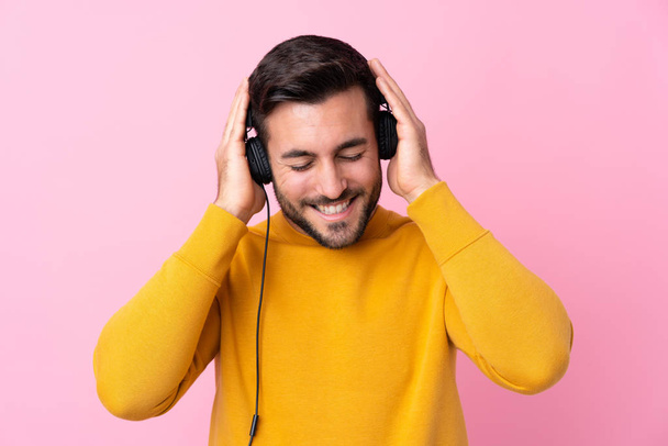 Молодий красивий чоловік з бородою слухає музику над ізольованим рожевим
 - Фото, зображення