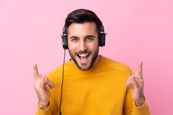 Young handsome man with beard listening music over isolated pink - Фото, изображение