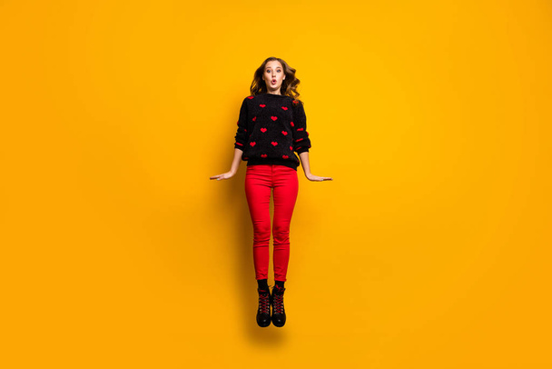 Full length photo of funny lady jumping up high spending free time weekend rejoicing wear hearts pattern sweater red trousers footwear isolated yellow color background - Fotó, kép