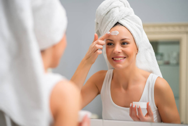 Ritratto di giovane donna che si applica la crema per la pelle sul viso
. - Foto, immagini