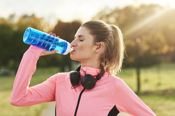 Mulher tomando um gole de água refrescante após o treinamento de jogging
 - Foto, Imagem