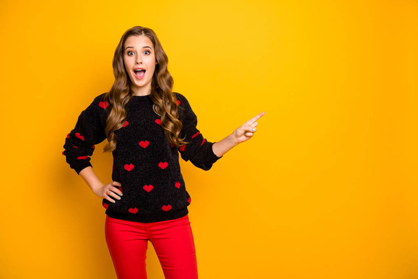 Photo of funny shocked lady open mouth indicating finger empty space advising low shopping season prices wear hearts pattern pullover red pants isolated yellow color background - Zdjęcie, obraz