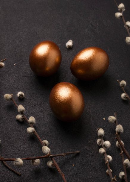 Huevos de Pascua de color cobre sobre un fondo negro cerca de ramas de sauce. Imagen vertical
 - Foto, imagen