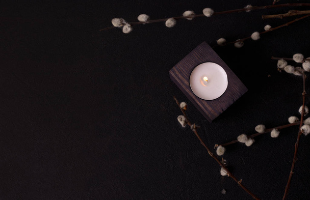 one candle in a wooden candlestick in willow branches on a black background. dark environmental design - Zdjęcie, obraz