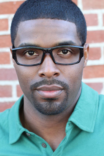 Szoros kép a fiatal fekete férfi visel szemüveg, nézi a kamera ellen tégla fal háttér - Fotó, kép