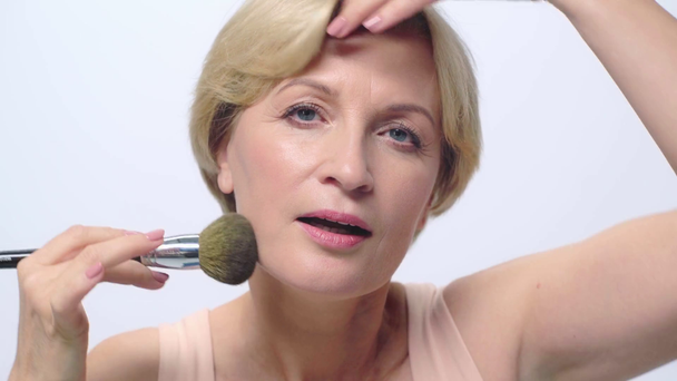 mature woman applying face powder isolated on white  - Footage, Video