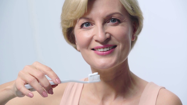 mujer alegre sosteniendo cepillo de dientes aislado en blanco
  - Imágenes, Vídeo