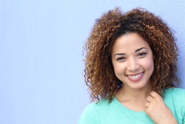 Latynoska dziewczyna z blond afro fryzura uśmiechnięty portret na niebieskim tle z miejsca kopiowania - Zdjęcie, obraz