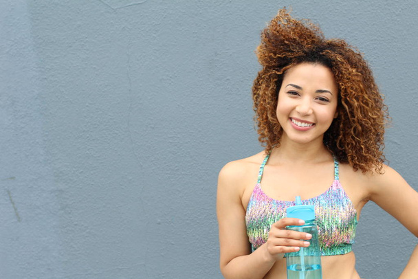 Szoros portré egy boldog fiatal nőről, aki vizes palackkal mosolyog. - Fotó, kép