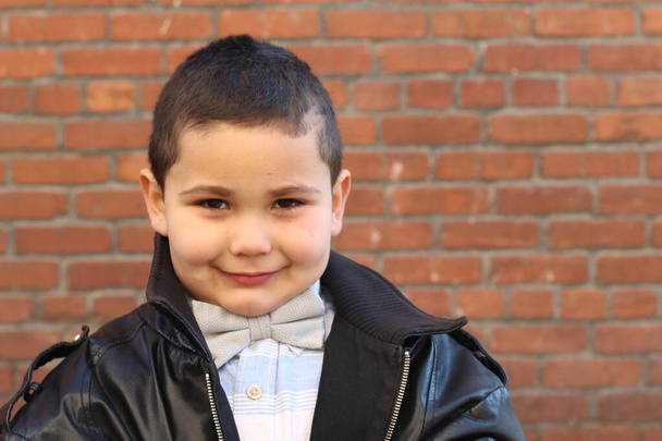 Εξωτερικό πορτρέτο του χαριτωμένο μικρό αγόρι ακρόαση παπιγιόν και μαύρο δερμάτινο μπουφάν - Φωτογραφία, εικόνα