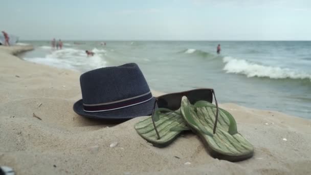 Αξεσουάρ για την παραλία ξαπλωμένη στην άμμο, ανδρικές παντόφλες και γυαλιά ηλίου στην άμμο της παραλίας - Πλάνα, βίντεο