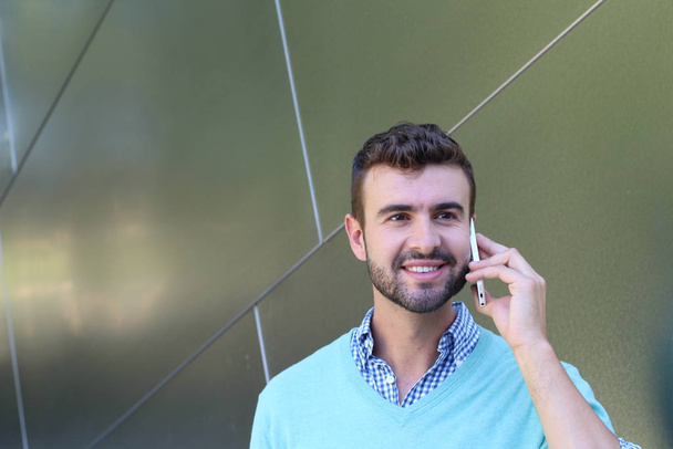 Portrait of young man in checked shirt and cyan sweater talking on phone  - Photo, Image