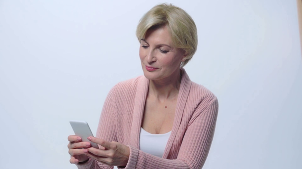 happy mature woman using smartphone isolated on white  - Кадри, відео