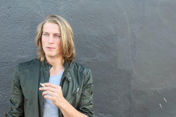 close-up portrait of handsome young stylish man with long hair smoking cigarette on street - Photo, image