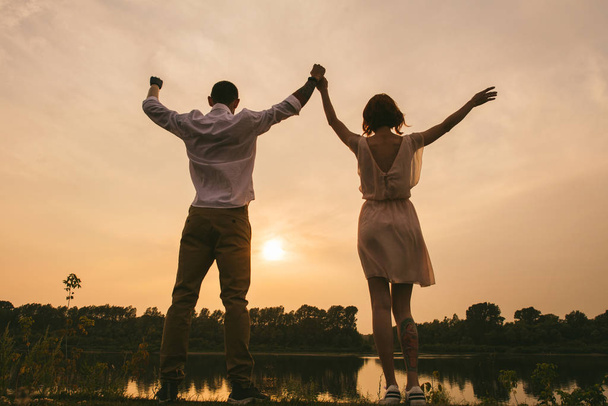 Couple standing on a river shore, celebrating a beautiful sunset taking place. - Foto, immagini