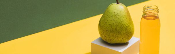 fresh juice in bottle near pear and white cube on green and yellow background, panoramic shot - Фото, изображение