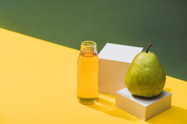 friss gyümölcslé palackban, körte és fehér kockák közelében, zöld és sárga alapon - Fotó, kép