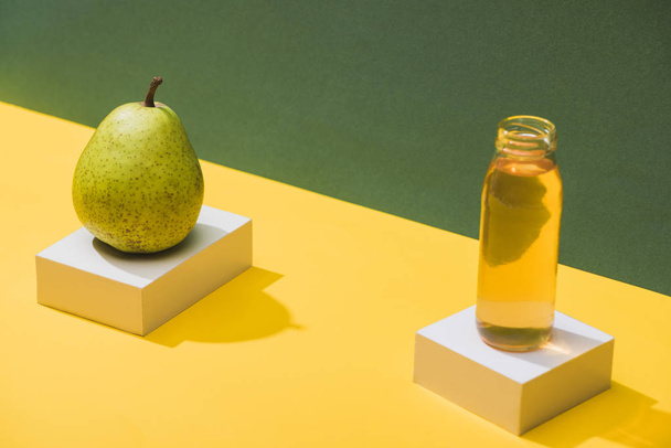 fresh juice in bottle near pear and white cubes on green and yellow background - Φωτογραφία, εικόνα