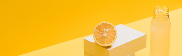 fresh juice in bottle near lemon and white cubes on yellow background, panoramic shot - 写真・画像