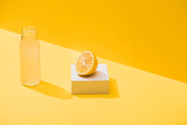 fresh juice in bottle near lemon half and white cube on yellow background - Fotó, kép