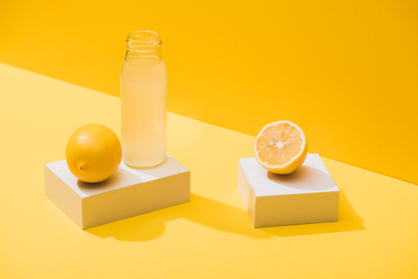 čerstvá šťáva v láhvi v blízkosti citrony a bílé kostky na žlutém pozadí - Fotografie, Obrázek