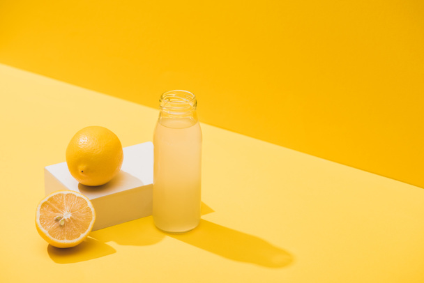 fresh juice in bottle near lemons and white cube on yellow background - Fotoğraf, Görsel