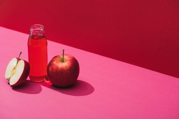 friss gyümölcslé üvegben, vörös és rózsaszín hátterű alma közelében - Fotó, kép