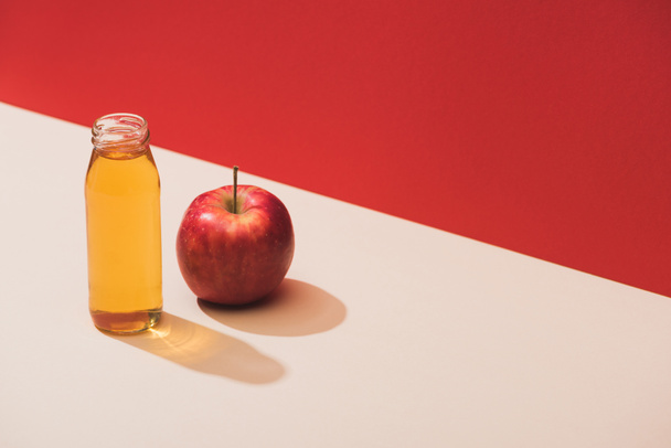 fresh juice in bottle near apple on red background - Фото, зображення