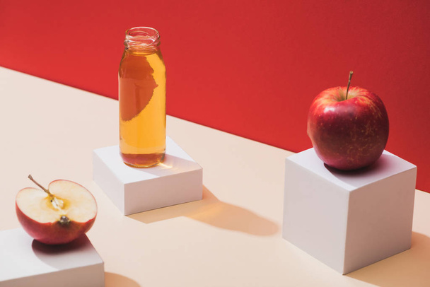 fresh juice in bottle near apples and white cubes on red background - Valokuva, kuva