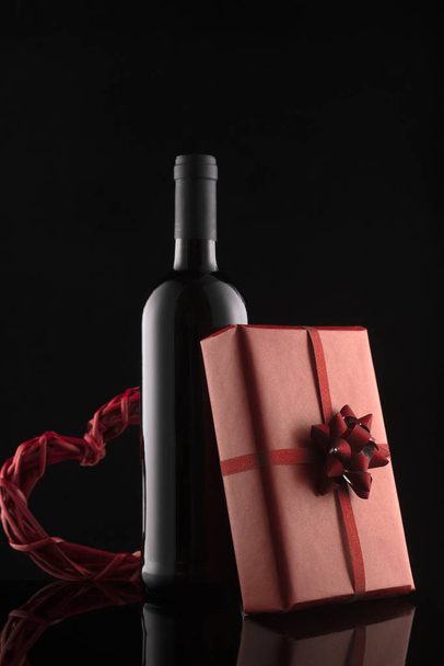 Gift box, wine bottle and red hearts on black background. - Photo, image