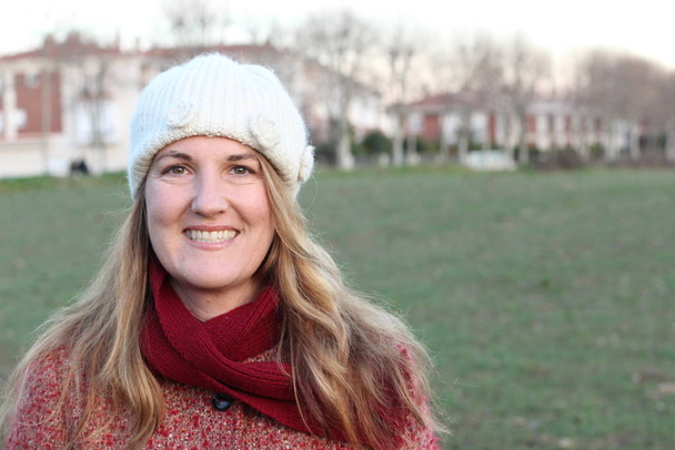 Retrato de una mujer rubia sonriente con ropa de invierno de pie en el parque durante el día
 - Foto, Imagen