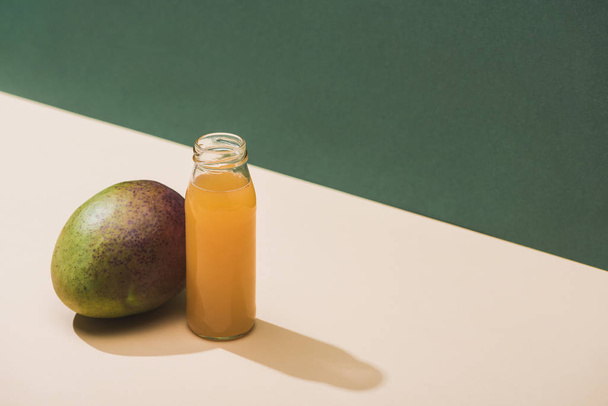 fresh juice in bottle near mango on green background - Φωτογραφία, εικόνα