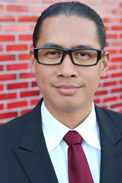 close-up retrato de belo jovem empresário asiático em terno e óculos na frente da parede de tijolo vermelho
 - Foto, Imagem