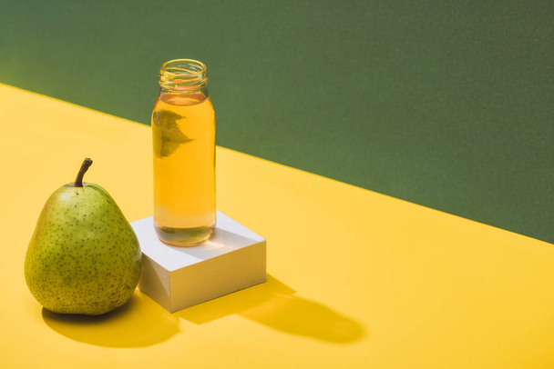 fresh juice in bottle near pear and white cube on green and yellow background - Fotó, kép