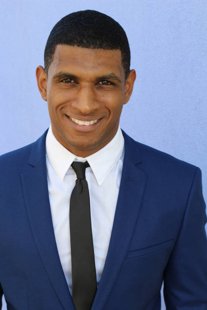 close-up portrait of handsome young african american businessman in suit in front of blue wall - Photo, Image