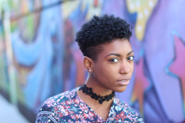 Beautiful African woman with short curly hair standing outdoors on graffiti background - Photo, image