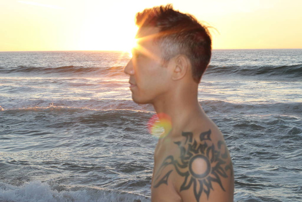 portrait of handsome young shirtless asian man on seashore at sunset - Foto, afbeelding