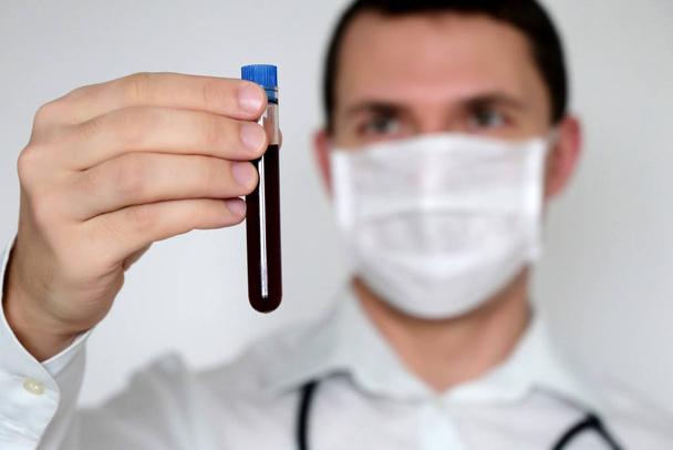 Test tube in male hand close up, doctor in medical mask holding a vial with red liquid. Concept of blood sample, vaccination, coronavirus, medical and chemical research, scientist - Photo, Image