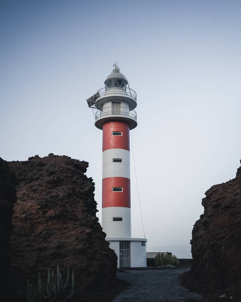 Vertical shot of the Punta Teno Lighthouse behind the rocks in Spain - Φωτογραφία, εικόνα