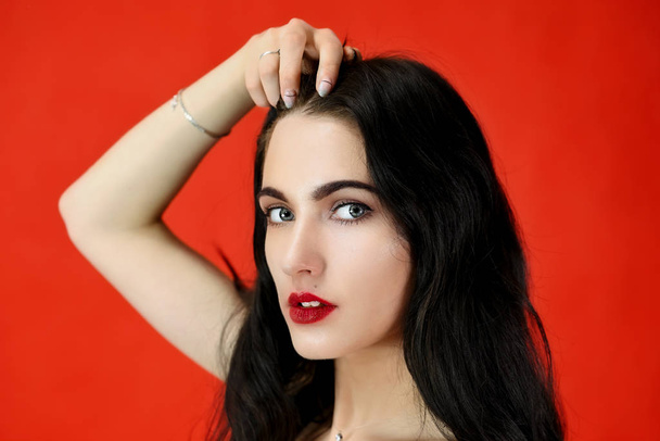 The concept of long beautiful hair. Close-up Portrait of a pretty brunette model girl with excellent makeup and luxurious hair on a red background in the studio. - Foto, imagen